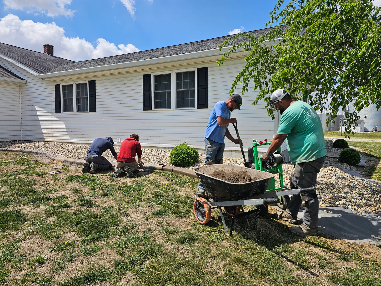 Stryker Outdoor Solutions team shaping concrete curbing beside a landscaped Southern Indiana home