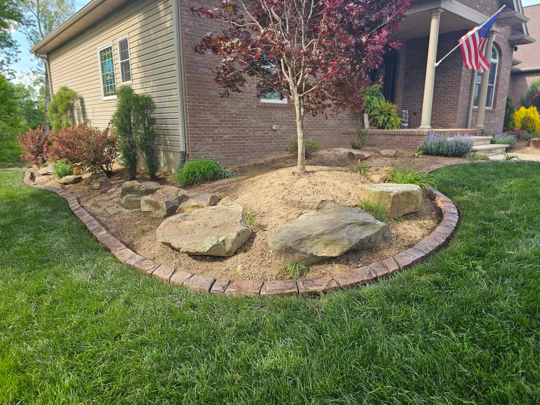 Natural-stone-style concrete border around a tree and boulder bed