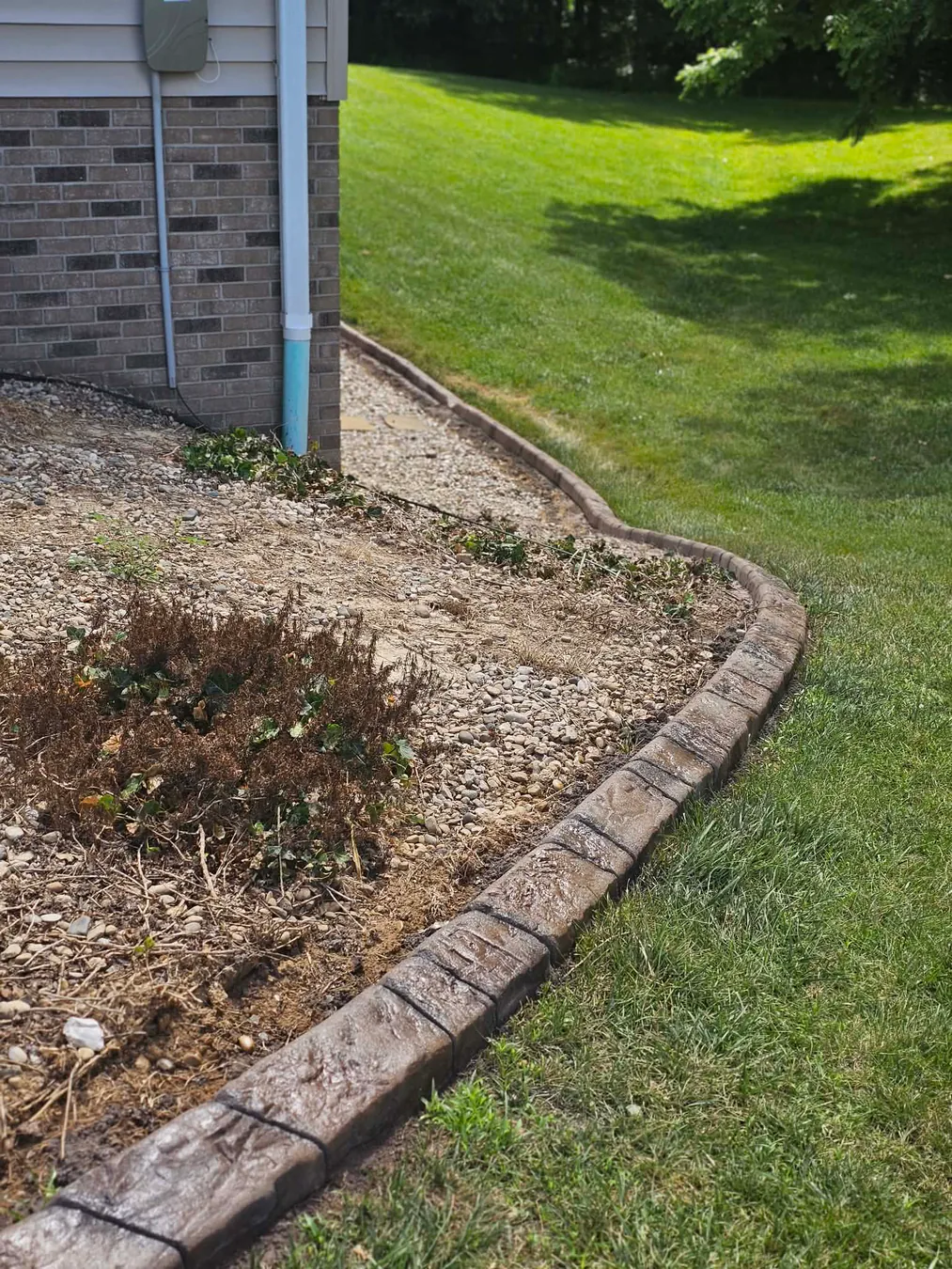 Long brick-look border following a backyard planting bed