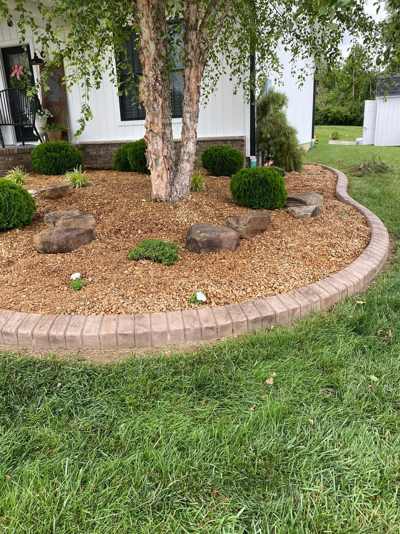 Finished farmhouse brick concrete curbing around a rock landscape bed with shrubs
